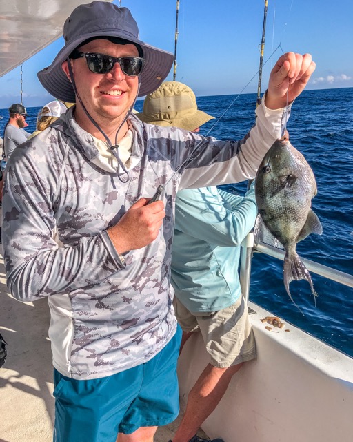 Man holding a triggerfish caught onboard a charter boat in Destin wearing a wide brim hat which is one of our beginner fishing tips